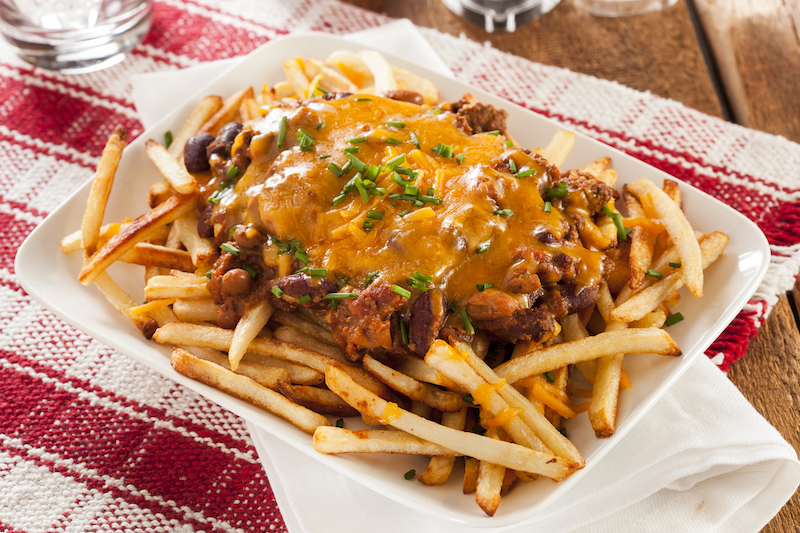Plate of chili cheese fries with melted cheddar and chopped herbs