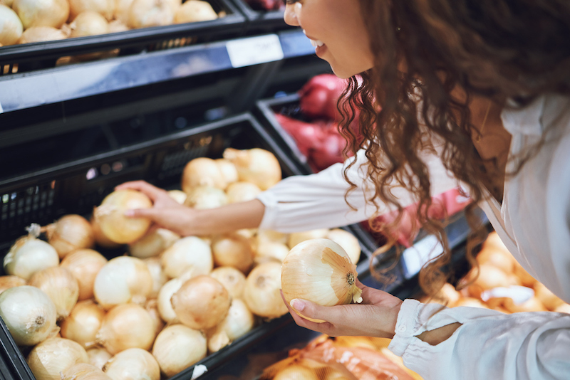 Person selecting onions in a grocery store produce section