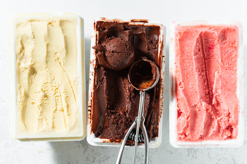 Vanilla, chocolate, and strawberry ice cream tubs with scooper