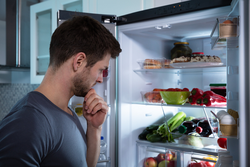 Man looking thoughtfully into an open refrigerator