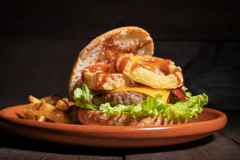 Burger topped with onion rings, lettuce, and sauce on a plate