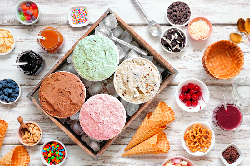 Assorted ice cream flavors with cones, sprinkles, and sweet toppings