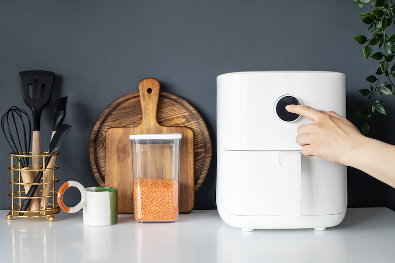 Person pressing button on a white air fryer in kitchen