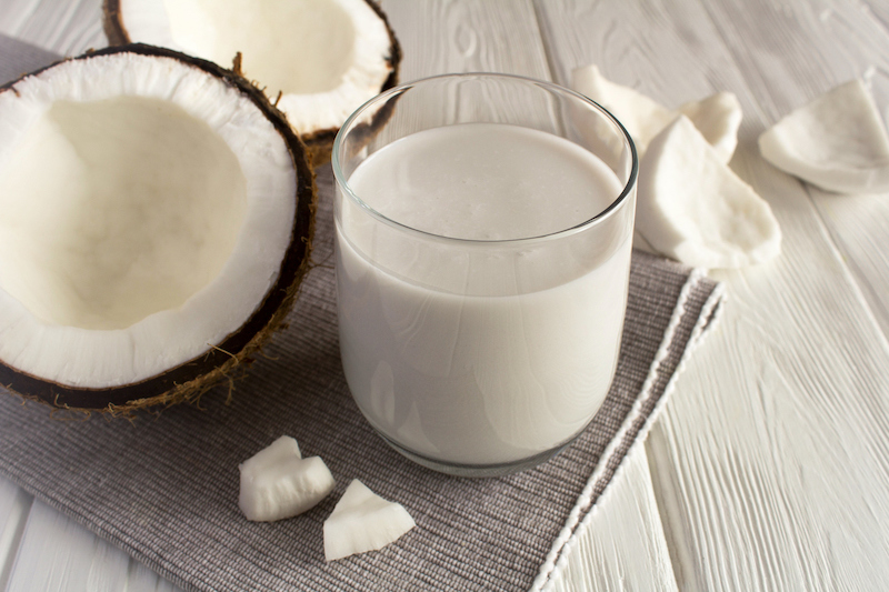 Glass of coconut milk next to fresh coconut pieces on a napkin