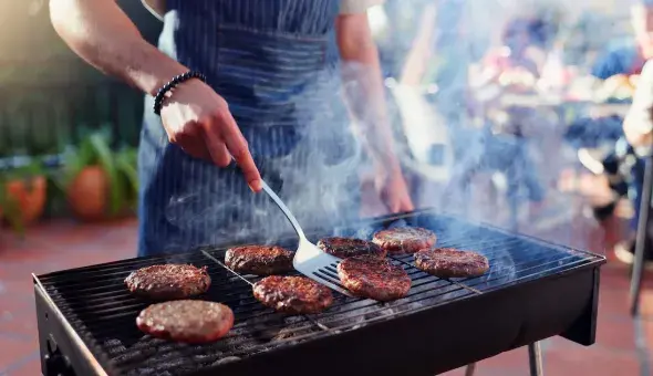 man flipping burgers on a grill outside